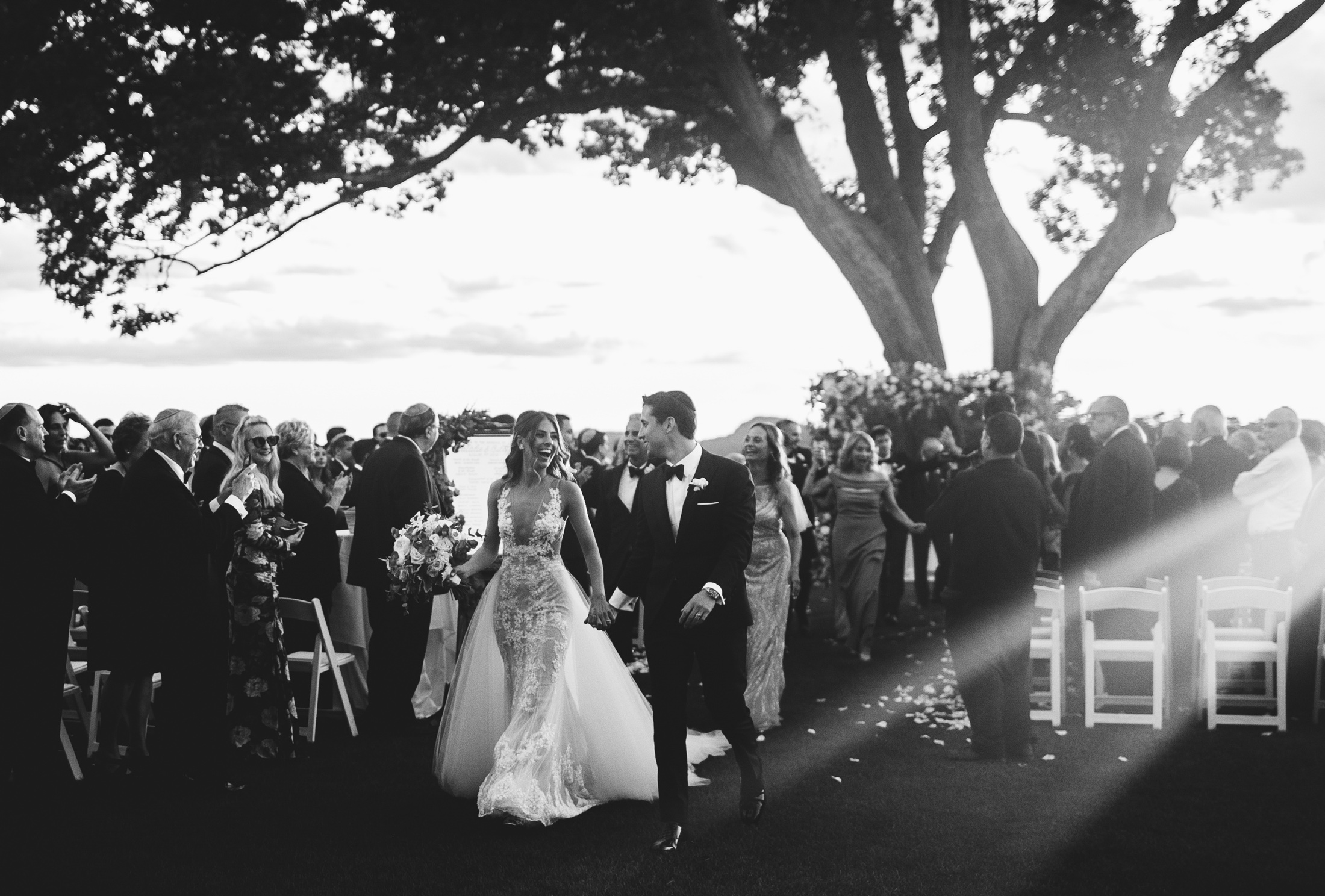 Black and white photograph of a couple walking the aisle through rays of light at Sleepy Hollow Country Club